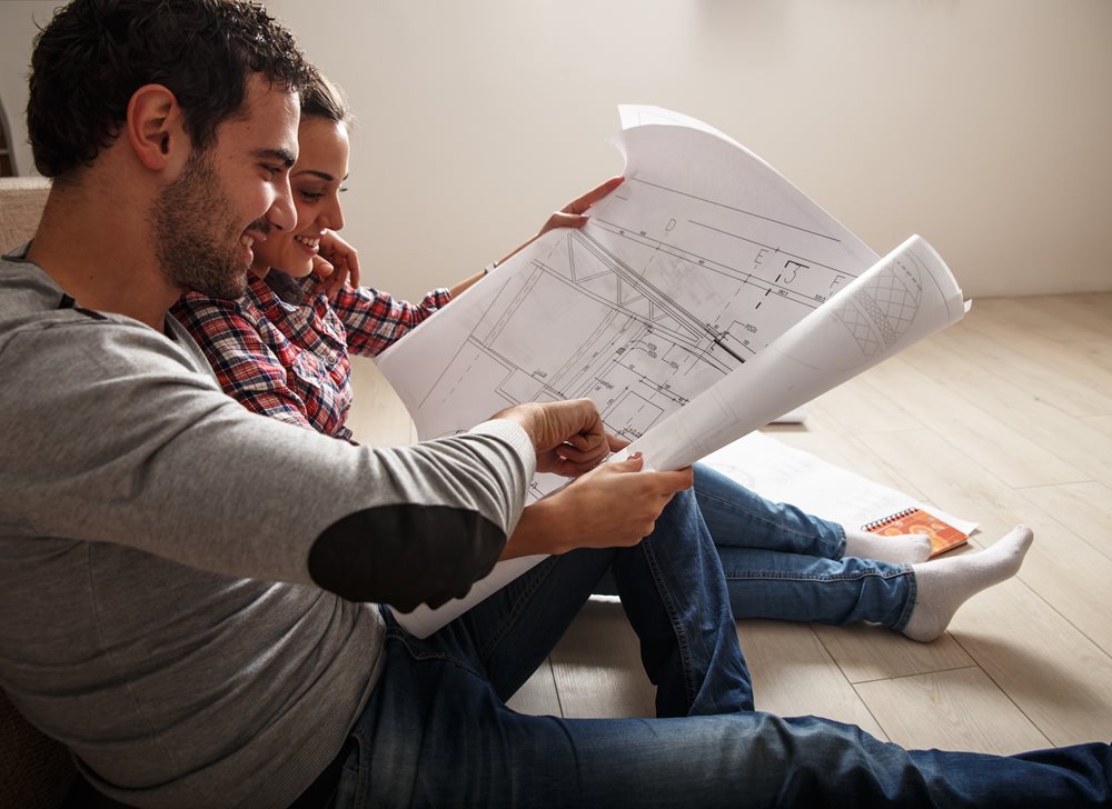 Man and women sitting on the floor holding a blue print drawing of a house